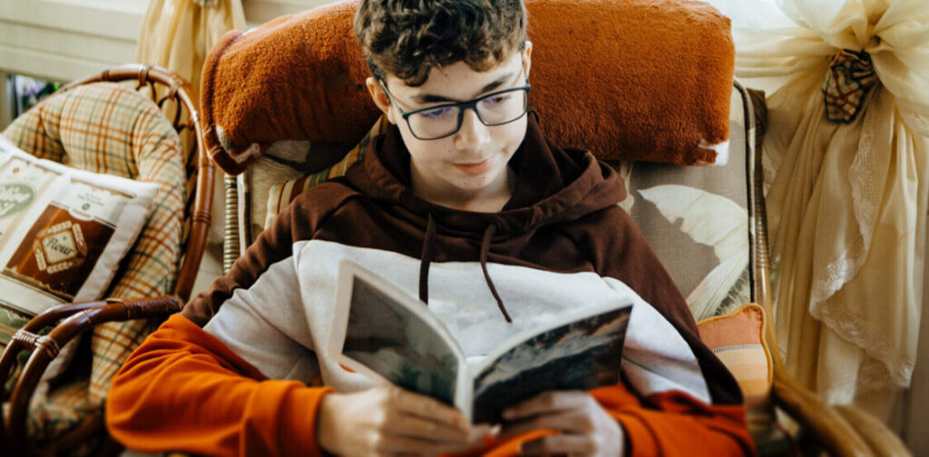 Niño adolescente hispano leyendo un libro en la sala de una casa
